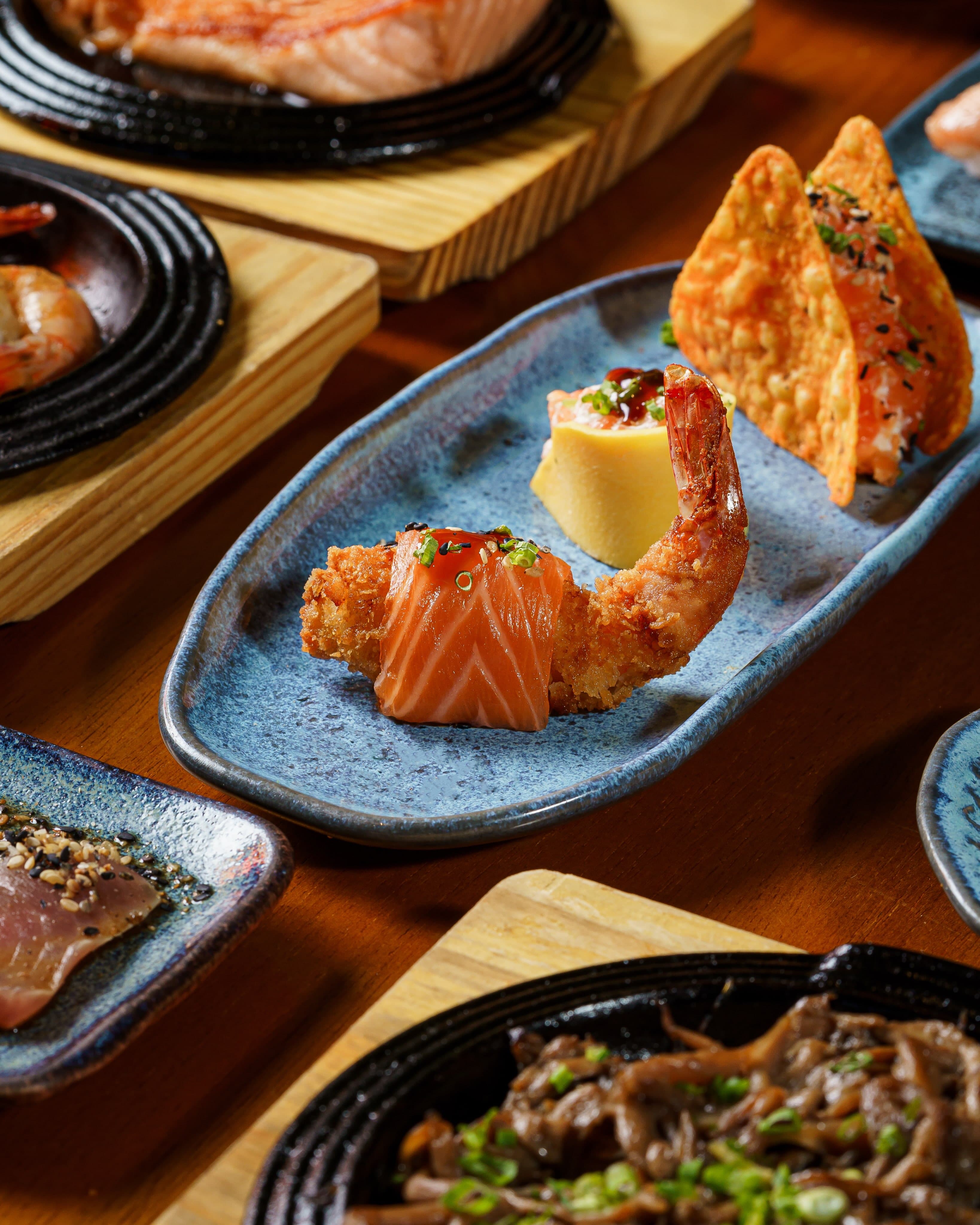 Pratos do rodízio na mesa: salmão com camarão, tamagoyaki e shimeji